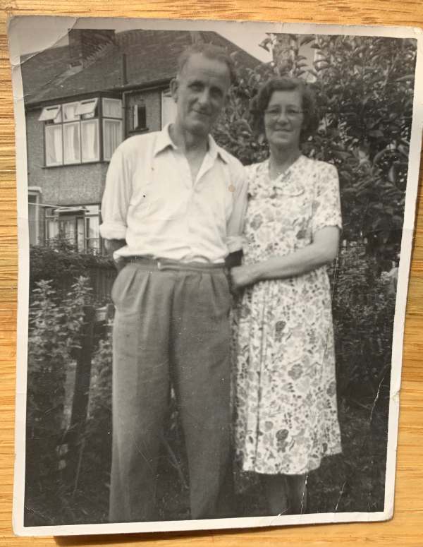 A black and white photograph ofSid and Dorothy in 1954(ish) standing arm in arm outside a semi-detached house.