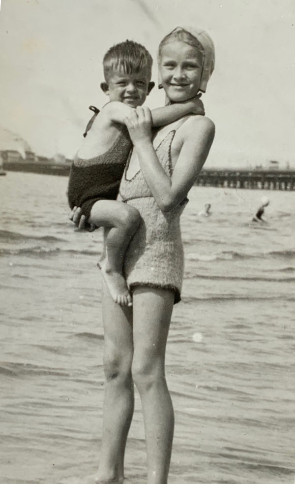 Bobby in his sister Wendy's arms. She is standing on the edge of the water, with what looks like Ryde Pier in the background.