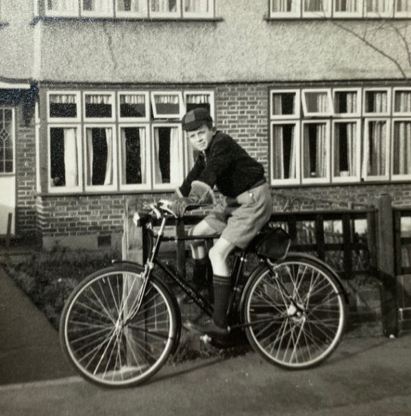 Bobby on a brand new bike outside his house. He is wearing his school uniform, complete with cap.