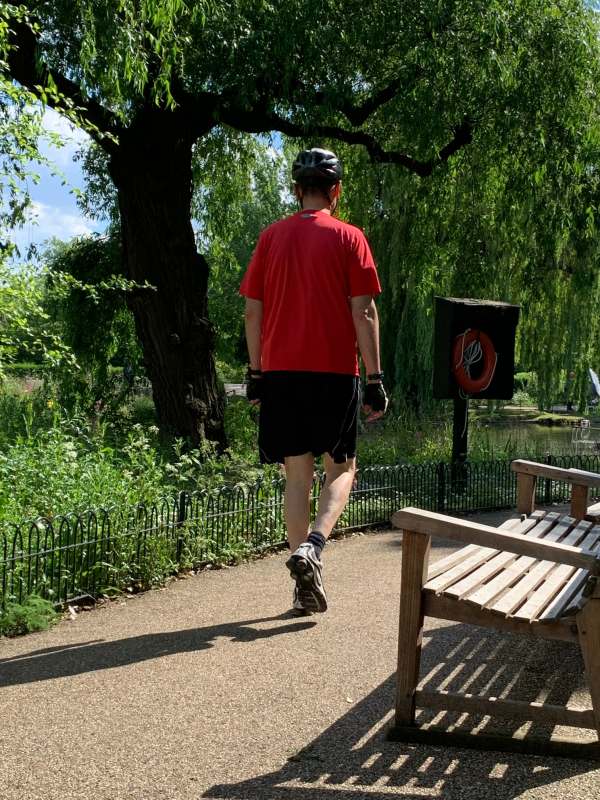 A man walking along the path by the lake, but wearing full cycling kit.