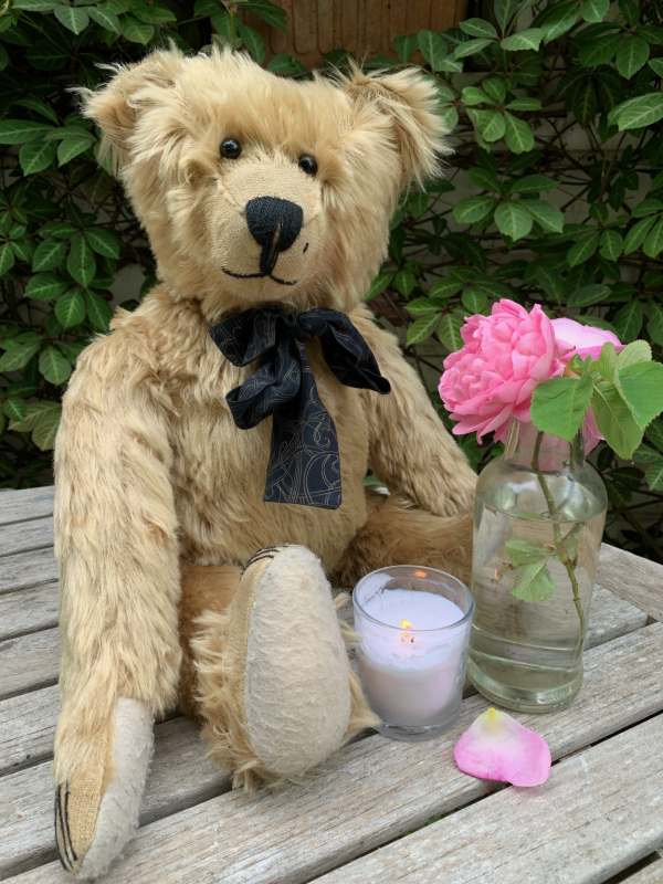 Bertie sat on an outdoor wooden table, along with a pink rose in a bottle and a lit candle in a glass.