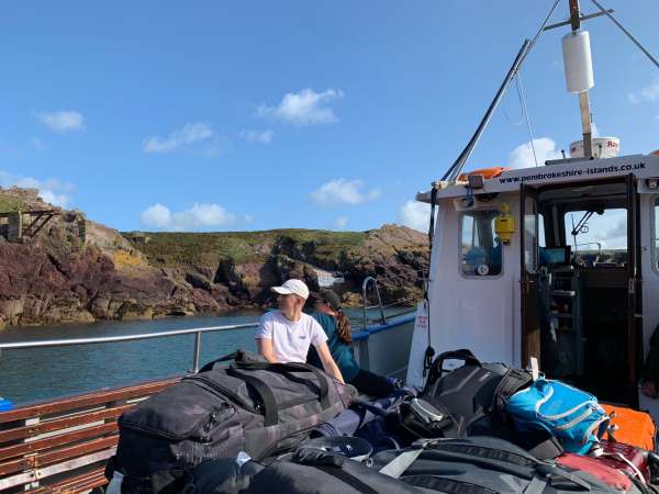 On the ferry. Two people, both called Sam, are viewed behind a big pile of luggage as they look back at the island.