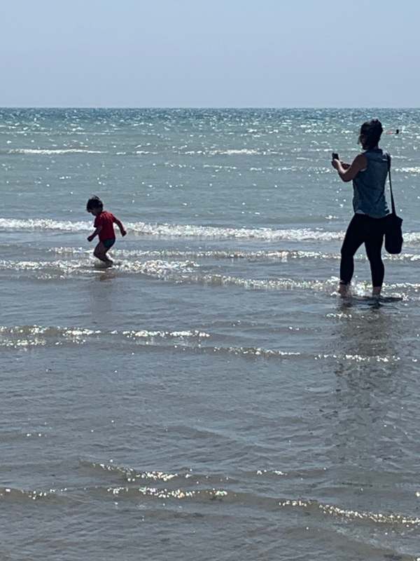 Little Jay playing in the water, while Jasmine watches on with her feet in the water.