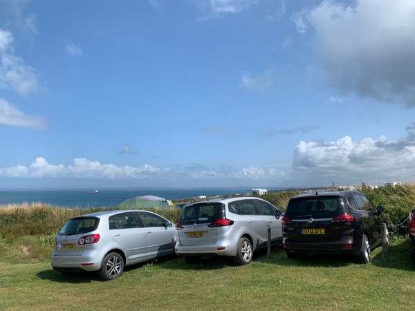 Three cars parked on grass overlooking the Pembrokeshire coastline.