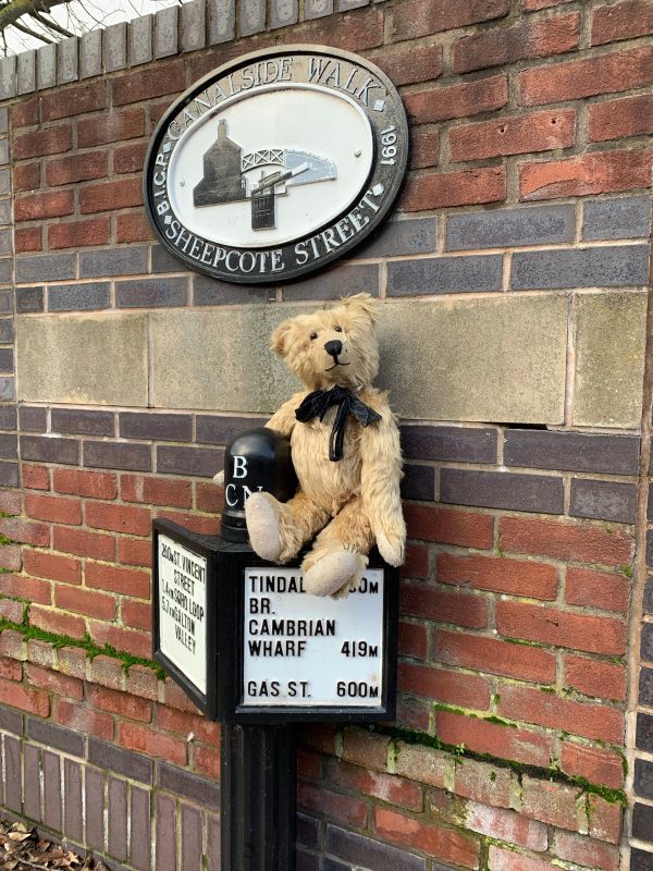 Bertie sat on a canal milepost underneath another sign that says "Canalside Walk Sheepcote Street"
