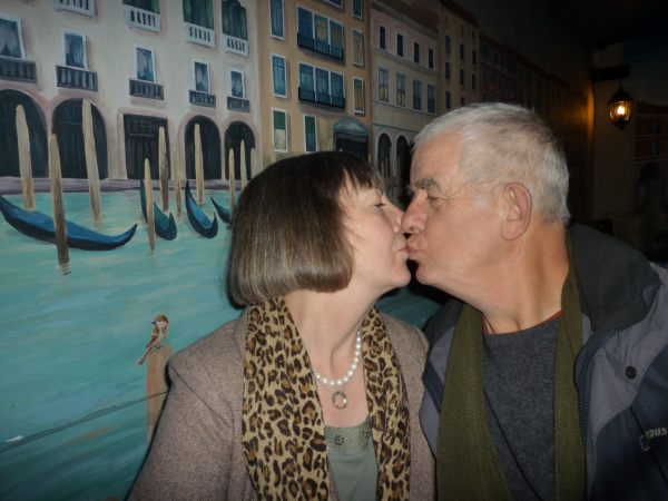 Bobby & Diddley sharing a kiss in front of a mural of Venice.