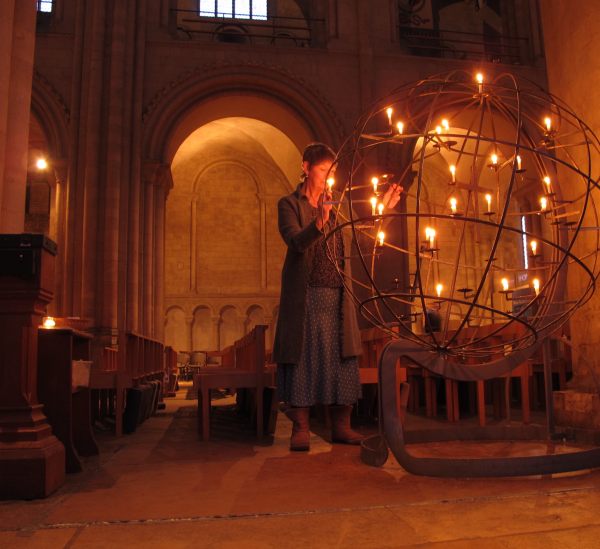 Diddley lighting a candle in an open wire globe inside a church.