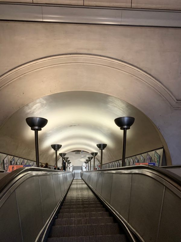 Tooting Broadway escalator. Central staircase with escalators either side. Chrome light stands.