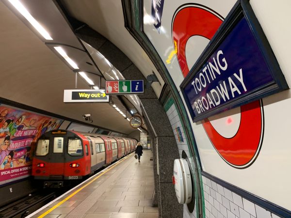 Platform at Tooting Broadway showing the roundel, with a train departing away from the camera.