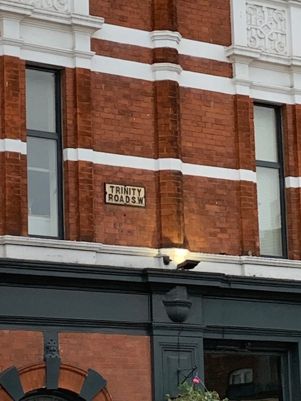 Road name sign "Trinity Road" on the side of the Wheatsheaf Pub opposite Tooting Bec Station.