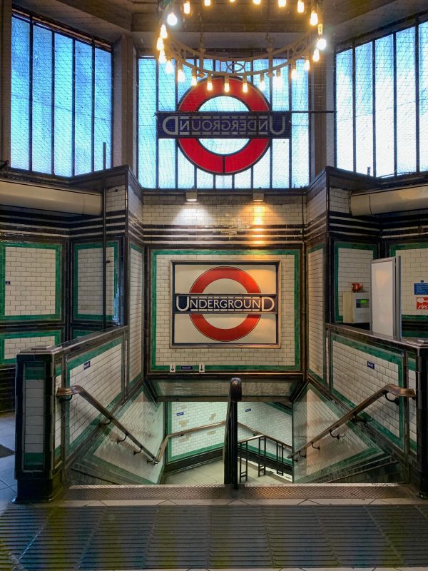 Stairway down in Tooting Bec Station, showing the rear of the roundel in the window, and another in tilework underneath.