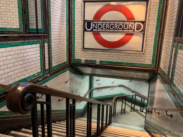 Close-up of the staircase and central mahogony handrail. The large, tiled Underground roundel looks over the scene.