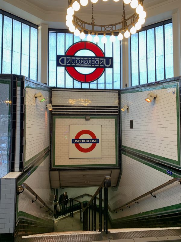 Stairway down in Tooting Bec Station, showing the rear of the roundel in the window, and another in tilework underneath.
