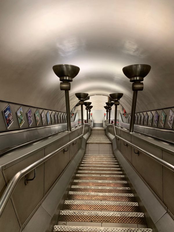 Balham Station escalator. Central staircase with escalators either side. Chrome light stands.