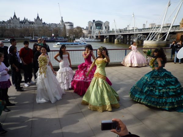 Lots of young ladies dancing on the promenade alongside the Thames. They are all in long, flowing dresses.