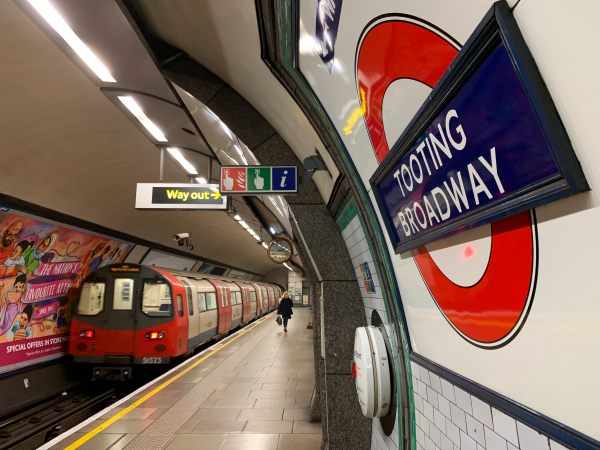 Interior of Tooting Broadway Underground Station, with a train pulling away from the platform.