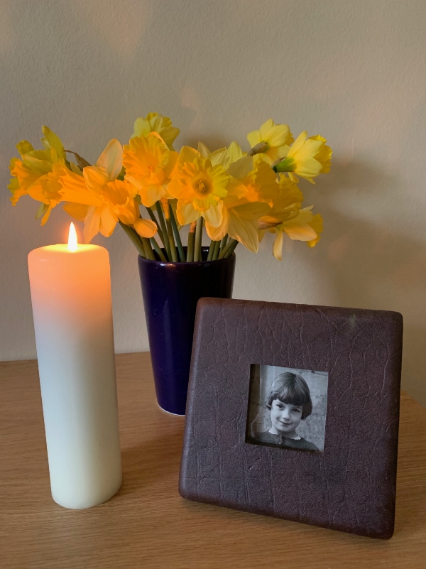 A lit candle, a bunch of daffodils in a vase alongside a picture of a young Diddley.