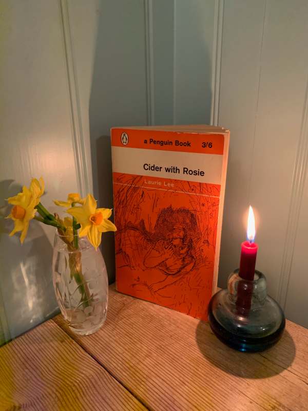 Lighting a Candle For Diiddley. The Penguin book "Cider with Rosie", flanked by a vase of daffodils and a lit candle.