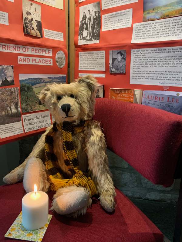 Bertie inside Slad Church sat on a red bench with a candle lit for Diddley.