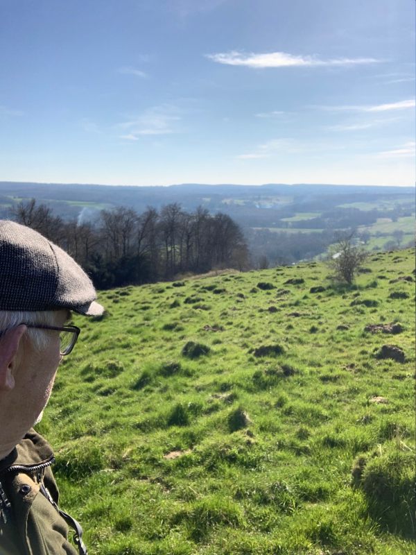 Bobby, wearing his cap, looking west to Blackdown across rolling green hills and fields.