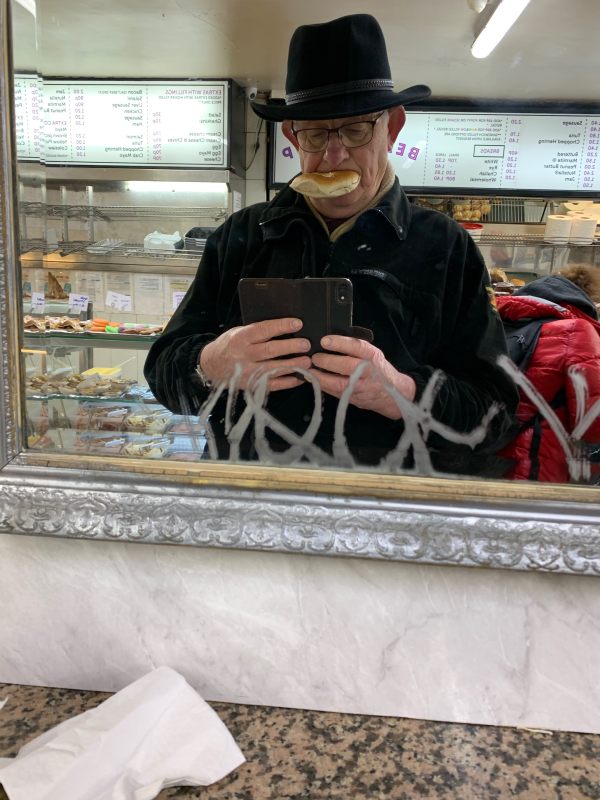 Bobby, using the mirror to surreptitiously take a selfie! He is wearing his hat and has a beigel stuffed in his mouth.