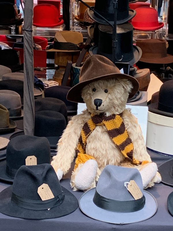 Close up of Bertie, wearing his Sutton United scarf and a hat, sat on the vintage hat stall in Spitalsfield Market.
