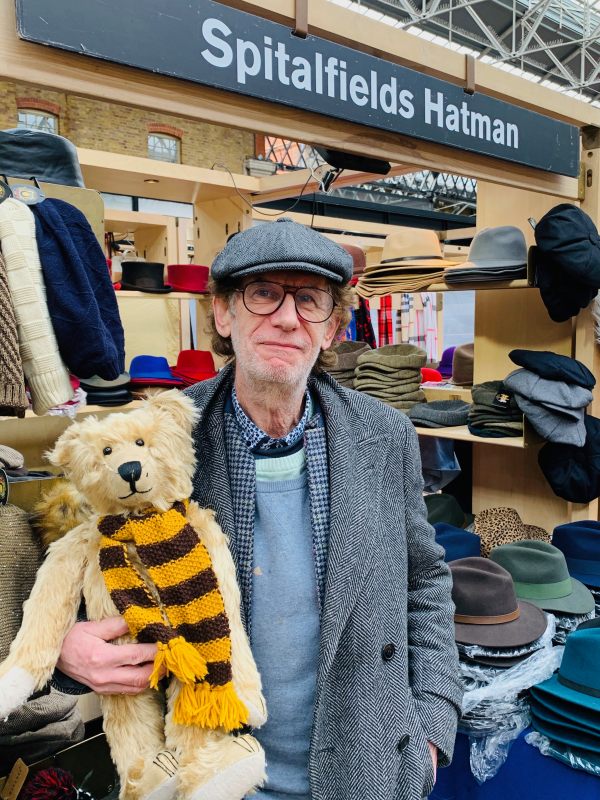 Bertie, wearing his Sutton United scarf, being held by the Spitalfields Hat Man, who is wearing a flat cap.