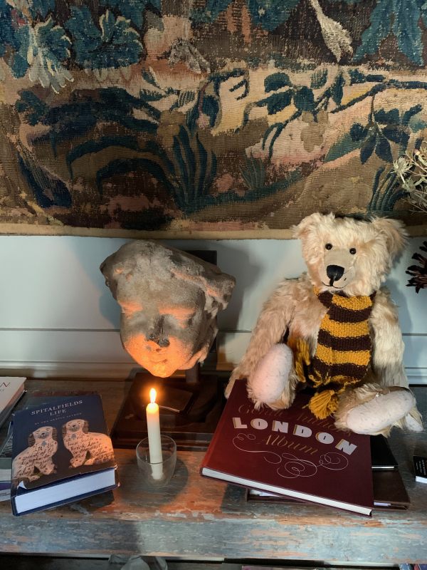 Candle lit for Diddley on top of a cupboard. There are some books on top, a gargoyle behind, and Bertie, wearing his Sutton United scarf. to the side.