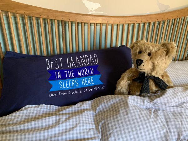 Bertie in a double bed alongside a pillow that reads "Best Grandad in the World sleeps here Love from Giselle and Daisy-Mae xx"