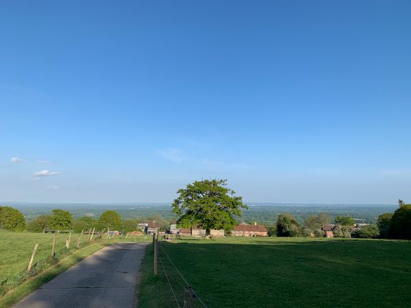 Looking down the North Downs. A very blue sky with ancient farm buildings and a few trees in the distance.