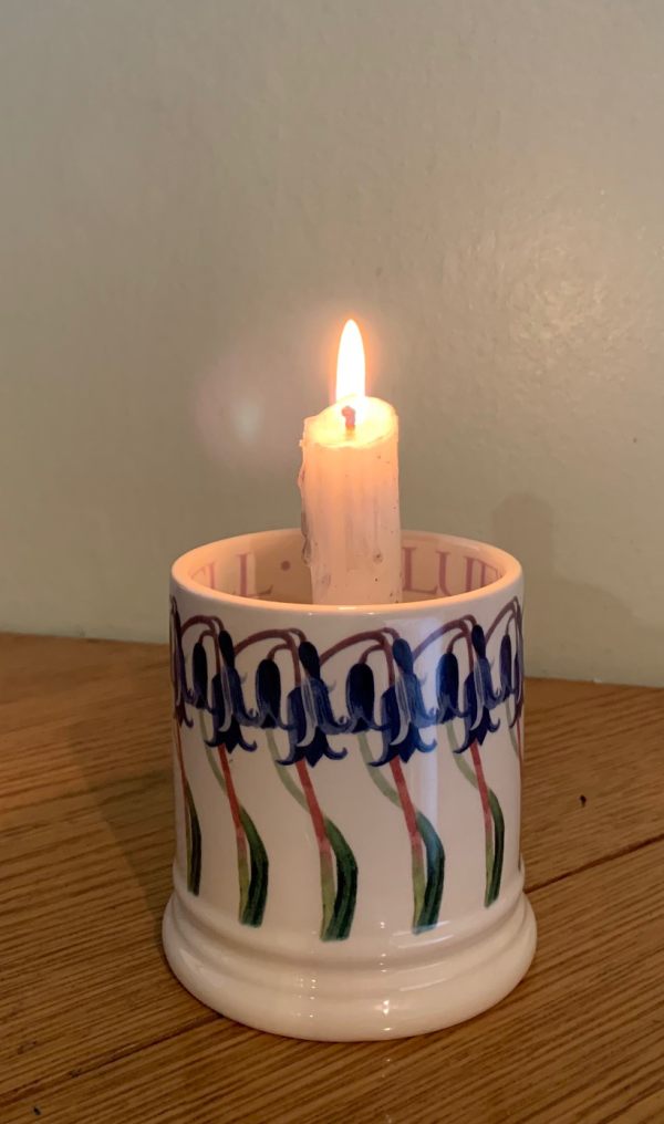 A candle lit for Diddley in a beautiful mug with painted Bluebells around the outside.