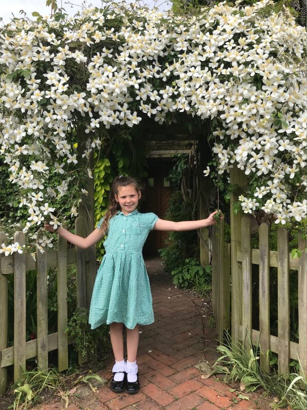 Kyla posing in front of the Clematis Montana wearing white ankle socks with black shoes and a summer dress.