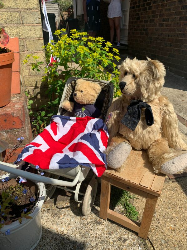 Bertie sat on a table in the garden at Laurel Cottage alongside another bear in a pram with a Union Jack flag draped over him.