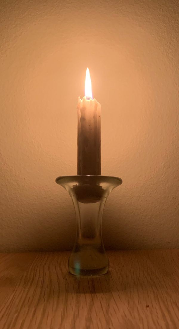 A candle lit for Diddley against a plain brown wall.