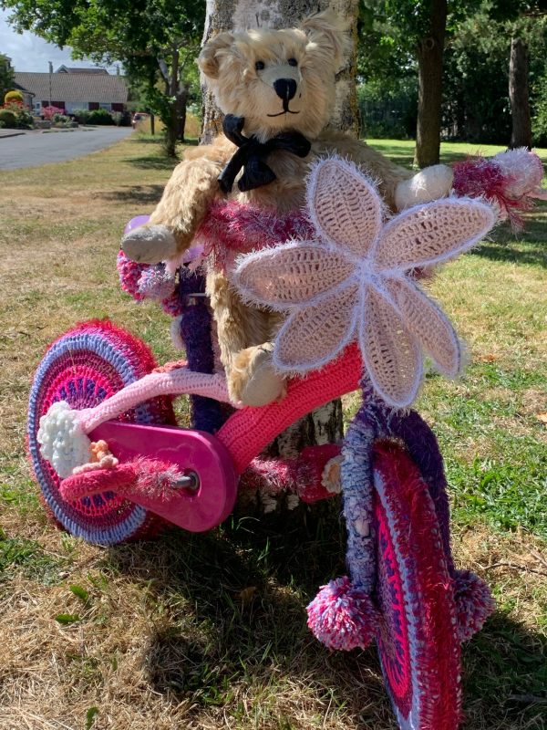 Yarnbomb Sisters - Bertie sat on a mainly pink knitted child's bicycle.