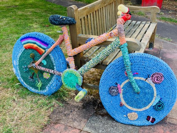 Yarnbomb Sisters - bright blue knitted bicycle with "NHS rainbow" on rear wheel.