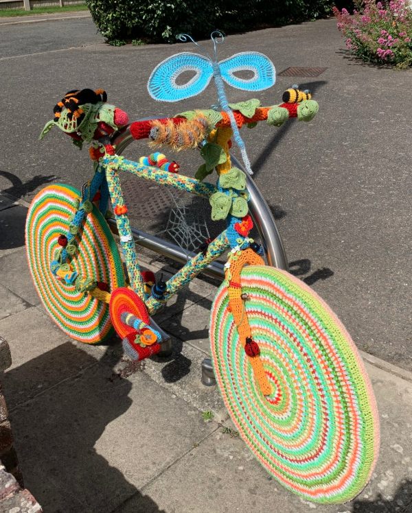 Yarnbomb Sisters - knitted bicycle with wheel rims in multi-coloured concentric circles and a butterfly on the handlebars.