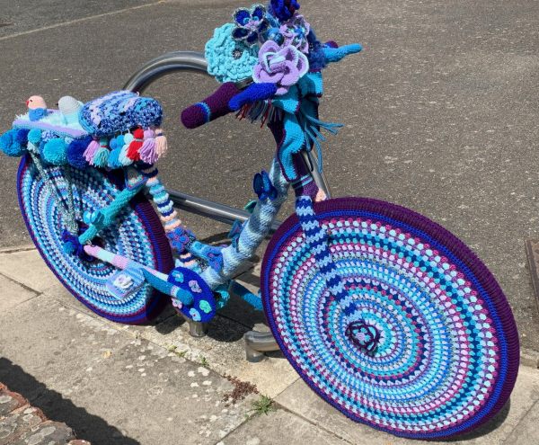 Yarnbomb Sisters - knitted bicycle with concentric circles of various shades of blues and purples on the wheels.