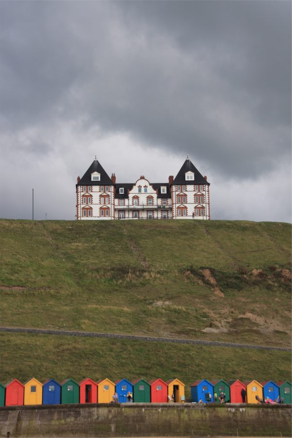 A large house on the cliffs at Whitby, with Beach Huts below.