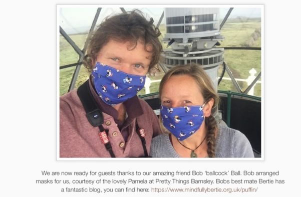 Richard and Giselle in their lighthouse home, pictured wearing facemasks. Underneath is the caption: "We are now ready for guests thanks to our amazing friend Bob "Ballock" Ball. Bob arranged masks for us, courtesy of the lovely Pamela at PrettyThings Barnsley. Bob's best mate Bertie has a fantastic blog, you can find here: https://www.mindfullybertie.org.uk/puffin/"