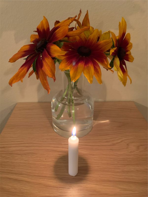 A candle lit for Diddley in front of a vase of Rudbeckias.