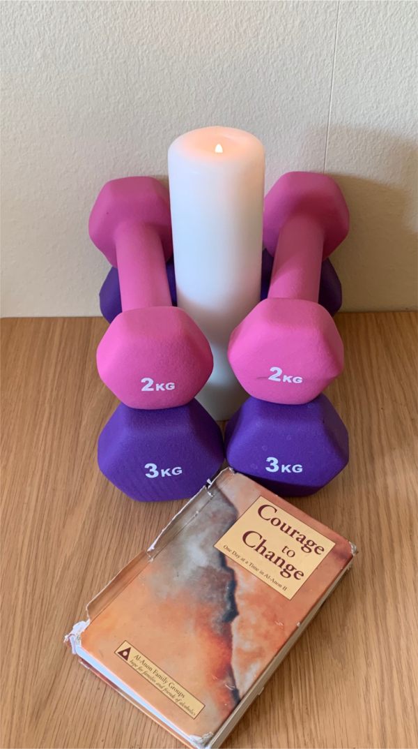 Two pairs of brightly coloured dumbells either side of a Candle Lit for Diddley. In front, is a copy of the book "Courage to Change".