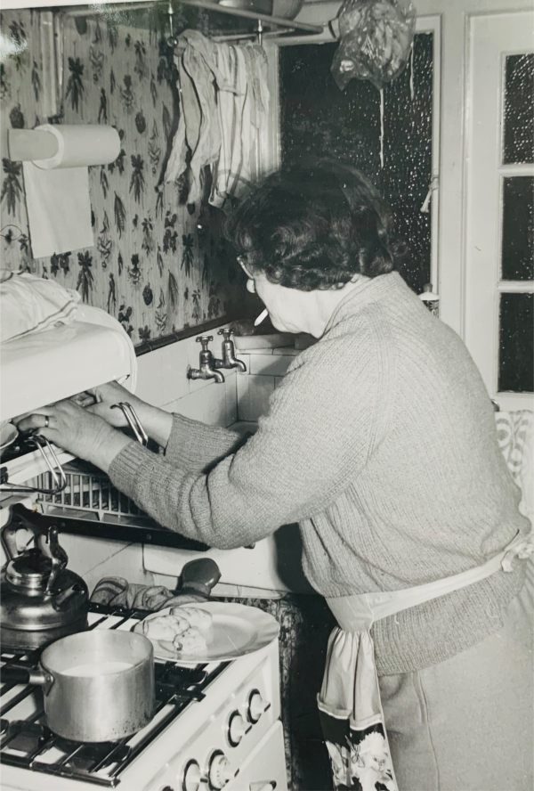 Time to Remember: Black & White picture of Bobby's Mum, Dolly, in the kitchen with her hands in the eye-level grill, cigarette in mouth.