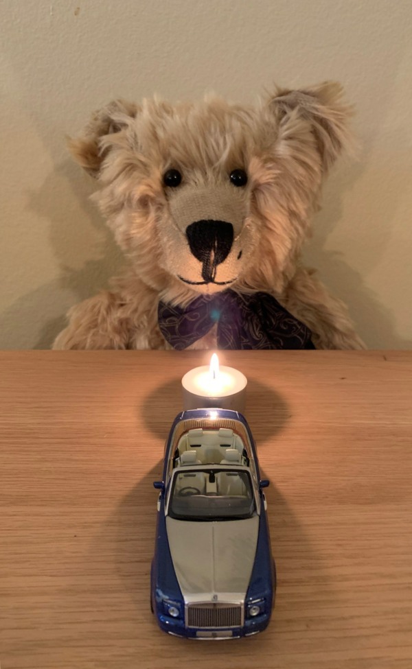 Bertie sat at a table facing a candle lit for Diddley, with a model of a Rolls-Royce in front.