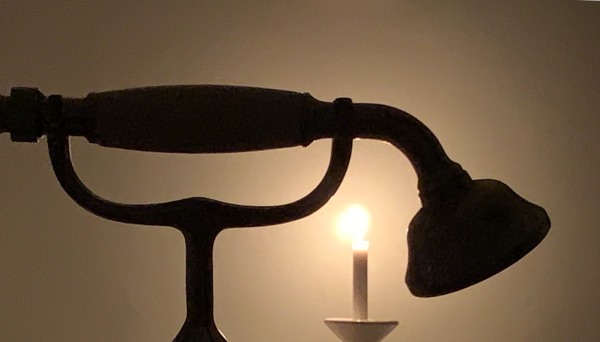 A candle lit for Diddley with the silhouette of an old-fashioned shower head.