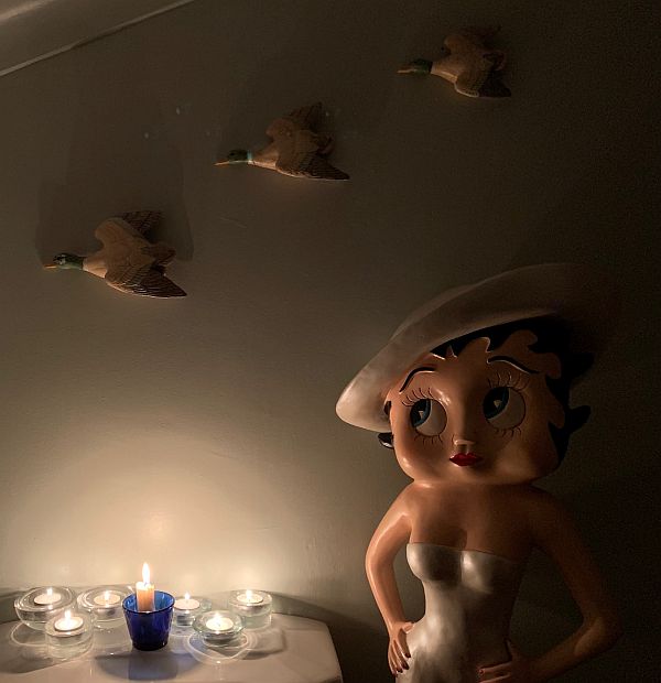 Betty, by a table with several candles lit for Diddley, under the three flying ducks on the wall.