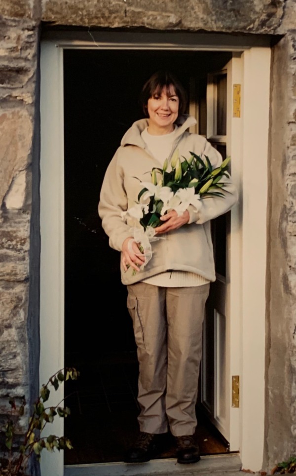 Bride Diddley (in hiking gear) in a doorway holding flowers.
