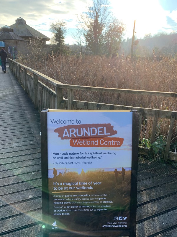 Sign "Welcome to the Arundel Wetland Centre", with some of the Wetlands in the background.