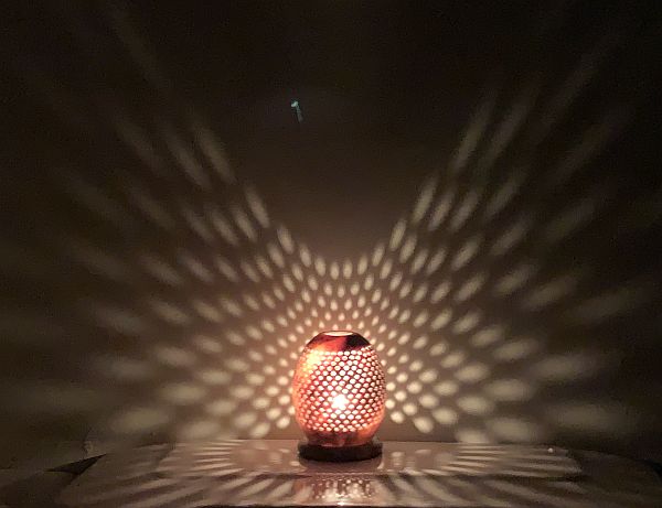 A candle lit for Diddley in a glass jar with diamond patterns which are cast up around the wall behind.