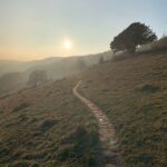 A gravel path along a hill slope with a misty sun in the background.